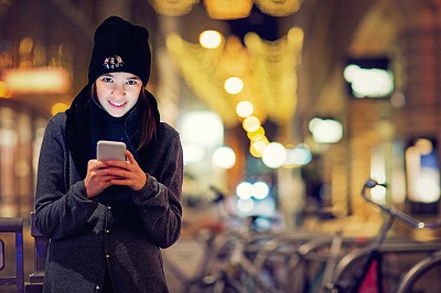 Mädchen in warmer Kleidung mit einem Mobiltelefon am Abend in einer Stadt Mädchen in warmer Kleidung mit einem Mobiltelefon am Abend in einer Stadt