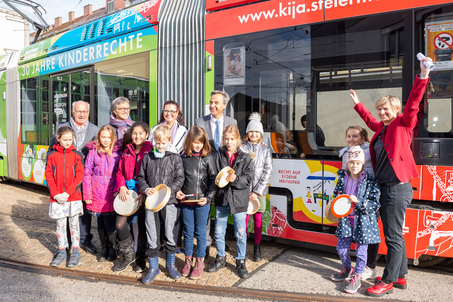 Kinderrechte sichtbar gemacht: Für ein halbes Jahr wird die Kinderrechte-Straßenbahn durch Graz fahren. Bürgermeister Siegfried Nagl (M.), Holding-Linien-Vorständin Barbara Muhr (r.), Ankünder-GF Dieter Weber (2. v. l.) und Karlheinz Herper (itglied des Menschenrechtsbeirates der Stadt Graz sowie Kinder- und Jugendanwältin Denise Schiffrer-Barac strahlten mit den SchülerInnen der VS Geidorf und der Sonne um die Wette. © Stadt Graz/Fischer Kinderrechte sichtbar gemacht: Für ein halbes Jahr wird die Kinderrechte-Straßenbahn durch Graz fahren. Bürgermeister Siegfried Nagl (M.), Holding-Linien-Vorständin Barbara Muhr (r.), Ankünder-GF Dieter Weber (2. v. l.) und Karlheinz Herper (itglied des Menschenrechtsbeirates der Stadt Graz sowie Kinder- und Jugendanwältin Denise Schiffrer-Barac strahlten mit den SchülerInnen der VS Geidorf und der Sonne um die Wette. © Stadt Graz/Fischer