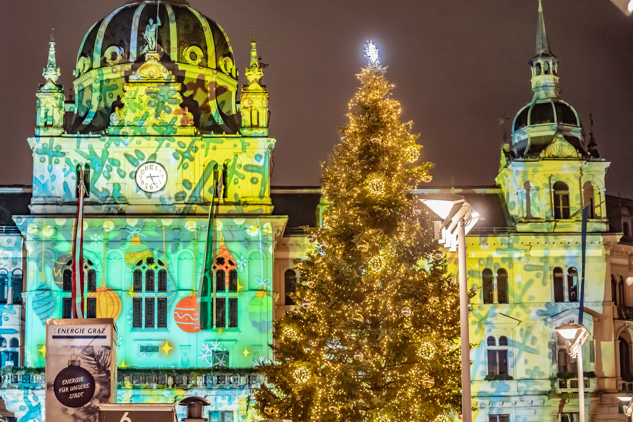 Der illuminierte Christbaum vor der weihnachtlichen Rathaus-Projektion.