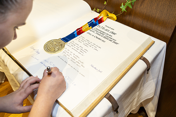 Eintragung ins Goldene Buch der Stadt. Neben den Unterschriften der Sänger:innen wurde auch ein Gedicht und die Zeichnung der Medaillen (unter der echten) hinterlassen.