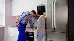 Ein Handwerker und eine Frau stehen in einer Küche. Der Handwerker repariert einen E-Herd.