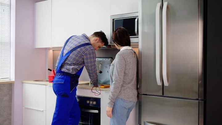 Ein Handwerker und eine Frau stehen in einer Küche. Der Handwerker repariert einen E-Herd.