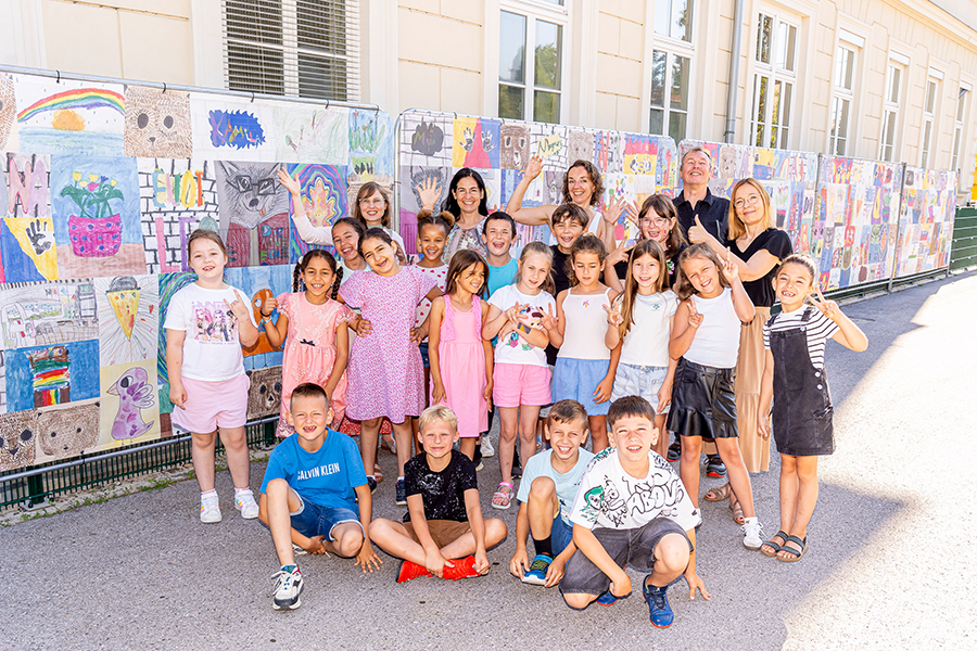 Bauzaun als Leinwand: Die Kids einer zweiten Klasse der VS Algersdorf vor ihren Kunstwerken