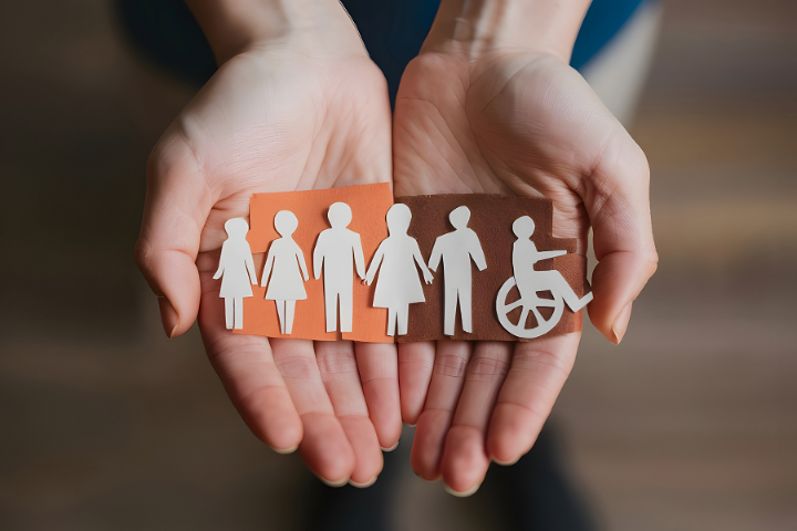 Zwei offene Hände halten stilisierte Figuren verschiedener Menschen, darunter eine Person im Rollstuhl © Adobe Stock/Leonardo Zwei offene Hände halten stilisierte Figuren verschiedener Menschen, darunter eine Person im Rollstuhl